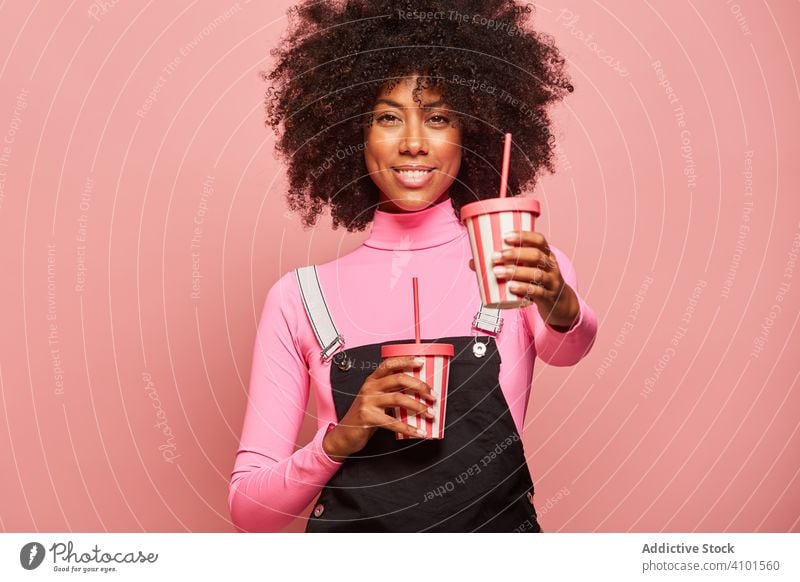 Glückliche schwarze Frau mit Einweg-Getränkebecher vor rosa Hintergrund trinken Tasse Stroh Afroamerikaner Lachen Einwegartikel heiter stehen gestikulieren