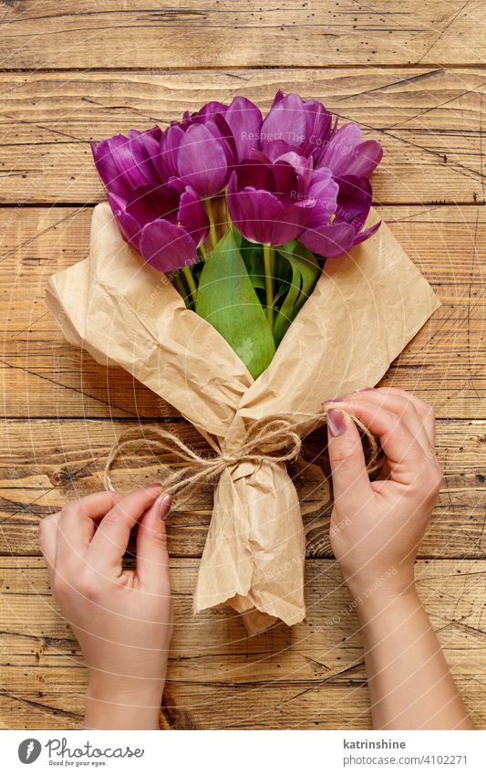 Hände mit lila Tulpen Bouquet in Handwerk Papier auf Holztisch Blumenstrauß purpur hölzern Draufsicht Halt Frühling Hochzeit Schleife vorbereiten kreieren