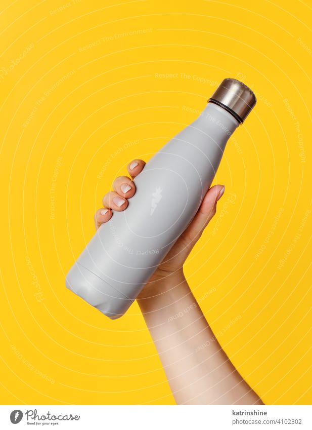 Hand mit grauer wiederverwendbarer Isolierflasche auf gelbem Hintergrund Flasche Attrappe isoliert ökologisch Wasser Stahl Thermo Leichtmetall blanko