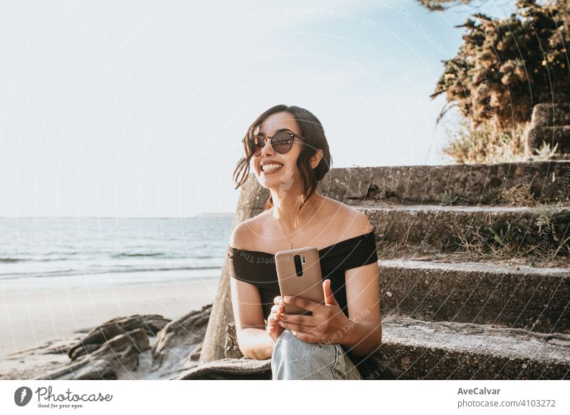 Junge Frau auf Sommerkleidung und Sonnenbrille mit seinem Telefon lächelnd mit Kopie Raum am Strand Afrikanisch Afro-Look Amerikaner Lächeln Person Gesicht