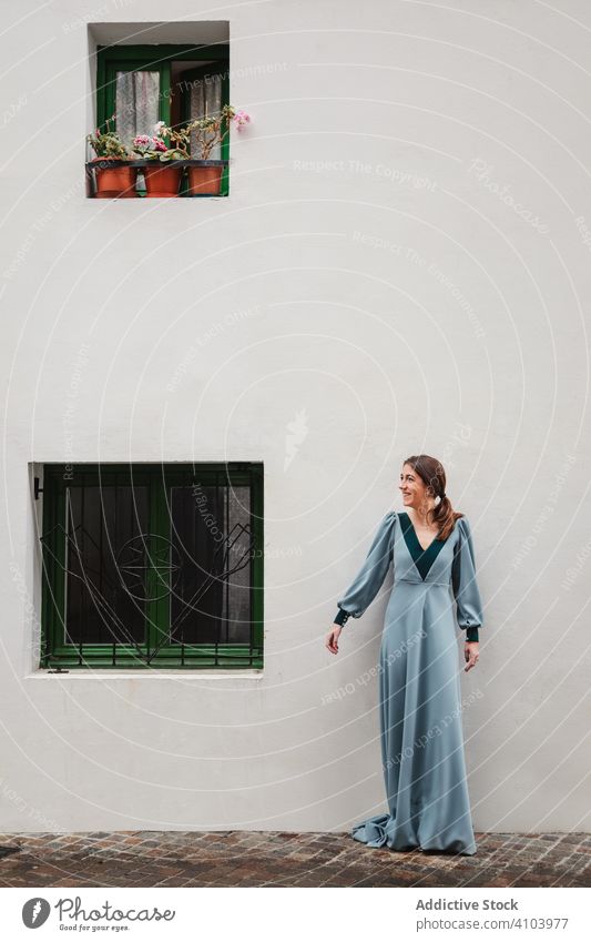 Fröhliche Frau im Retrokleid vor dem Haus Kleid altehrwürdig Lächeln Straßenbelag elegant Fenster Wand retro gealtert Außenseite Bekleidung Kleidungsstück