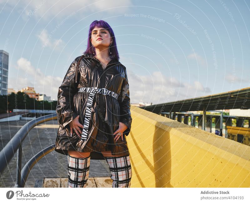 Frau mit violetten Haaren in der Nähe von Metallkonstruktionen stylisch urban purpur Frisur Jacke glänzend Zaun gelb Wand Mode jung Stil Model Straße menschlich