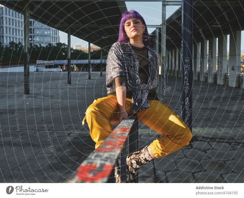 Frau mit lila Haaren in gelber Hose sitzt auf Metallzaun stylisch purpur Frisur glänzend Zaun Wand Mode jung urban Stil Model Straße menschlich Outfit Hipster