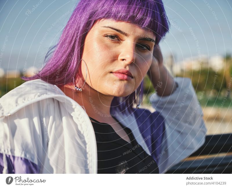 Frau mit violettem Haar lehnt an Metallzaun Lehnen berührend stylisch urban purpur Frisur Jacke glänzend Zaun Revier selbstbewusst Mode jung Stil Model Straße