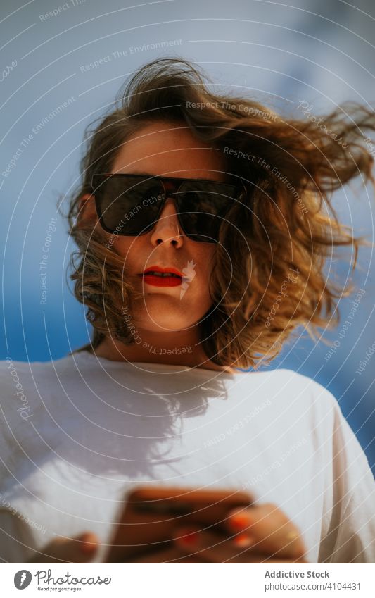 Modischer weiblicher Hipster mit Sonnenbrille und Smartphone Frau Stil benutzend Browsen blau Himmel Natur Urlaub Sommer rot Lippenstift Zeitgenosse aussruhen