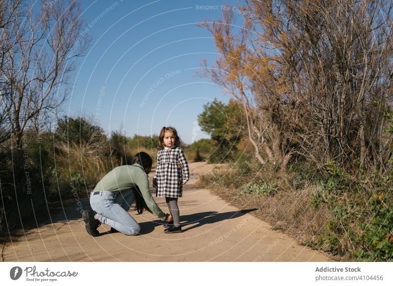 Mutter bindet Schnürsenkel für ihr Kind auf einem Weg auf dem Lande Kopplungsbindung Schuhbänder Mädchen Hilfsbereitschaft Tochter Landschaft Zusammensein