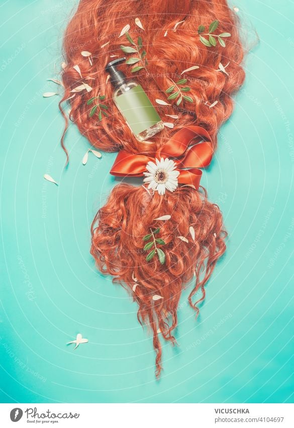 Rotes Ingwerhaar in einem Pferdeschwanz mit Band gebunden, grüne Blätter, Blumen und kosmetische Produktflasche : Shampoo, Haarspülung und Pflege auf türkisblauem Hintergrund. Schönheit und Haarstyling Konzept