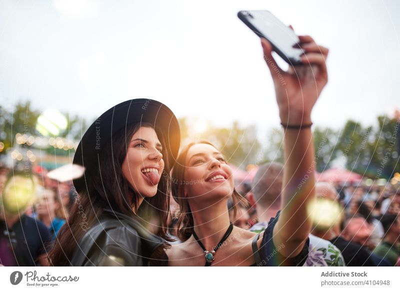 Fröhliche Frauen, die Selfies mit ihrem Smartphone machen, herumalbern und ihre Zungen in der Sonne herausstrecken Freund Stadtfest Feier Freundschaft