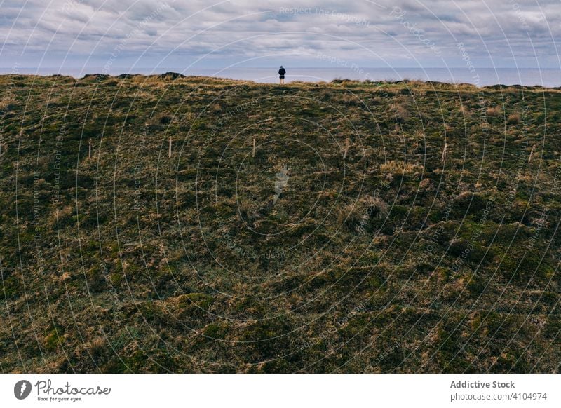 Einsame Person steht am Rande eines steilen Hügels aus grünem Lehm und schaut auf den Horizont Landschaft Tal pielagos Kantabrien Santander Spanien wolkig