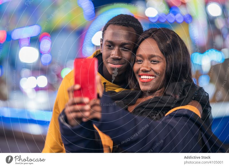 Schwarzes Paar macht Selfie auf dem Rummelplatz Messegelände Lächeln Smartphone ethnisch Nacht farbenfroh Illumination Entertainment Mann Frau Spaß Freund