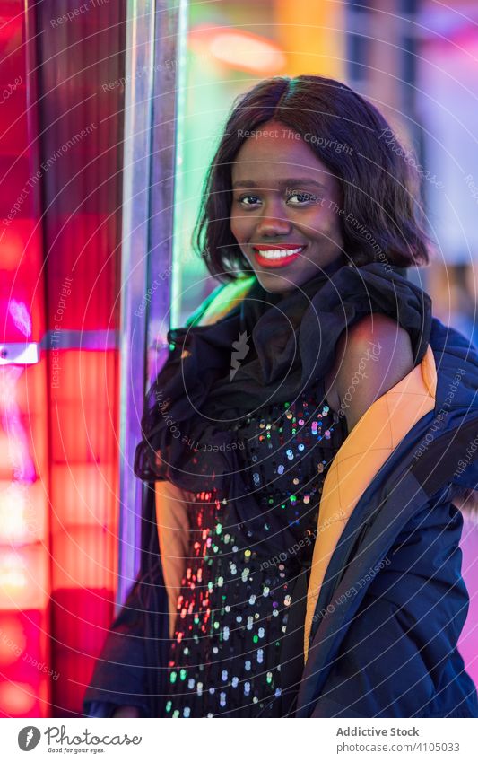Fröhliche schwarze Frau auf Rummelplatz Jahrmarkt Lächeln Nacht Arkaden Illumination Wochenende ethnisch Vergnügen Anziehungskraft farbenfroh Freude Glück