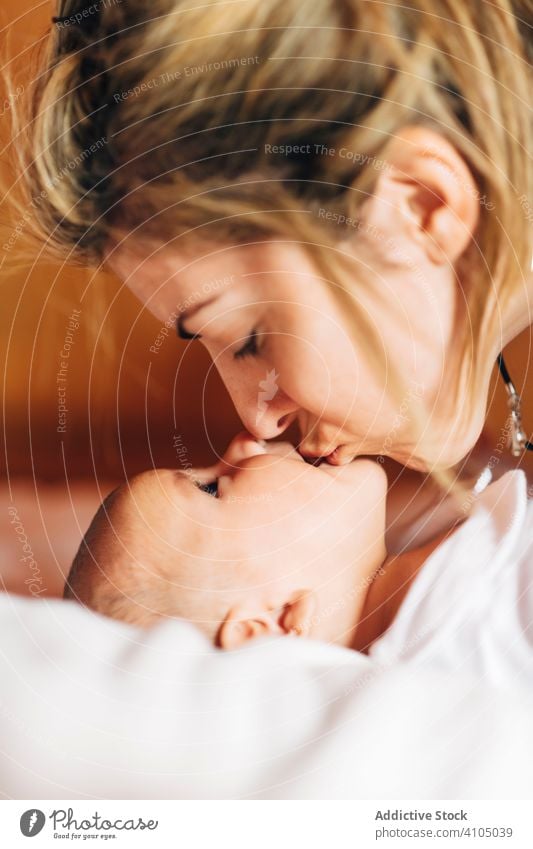 Strahlende Mutter berührt Nase an Nase des Babys spielen Glück Bonden Pflege neugeboren Zuneigung Lügen Bett heimwärts Säugling offener Mund berührende Nase