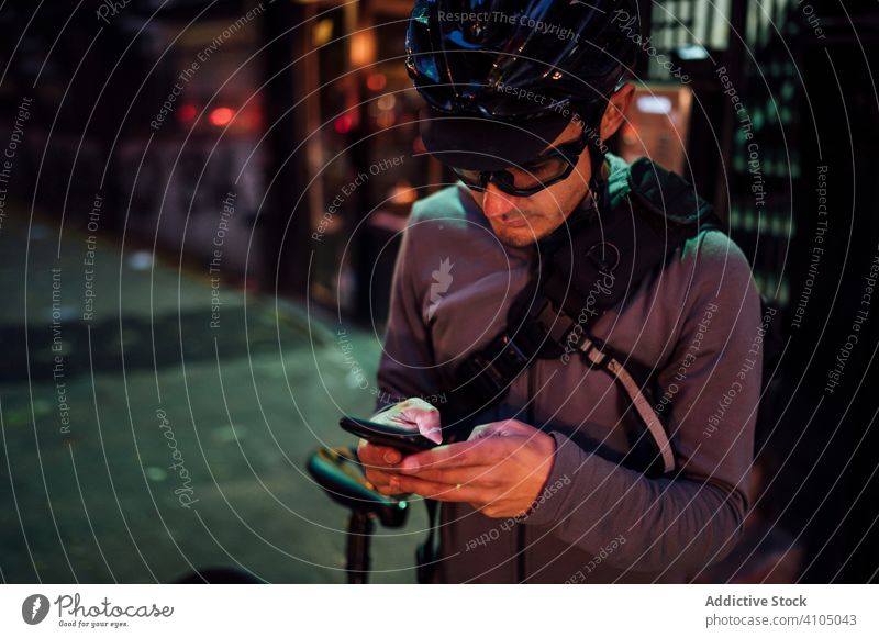 Profi-Radsportler mit Smartphone Mann Radfahrer benutzend Browsen Fahrrad Großstadt Handy Straße Asphalt Gerät Brille männlich Schutzhelm Sport Lifestyle