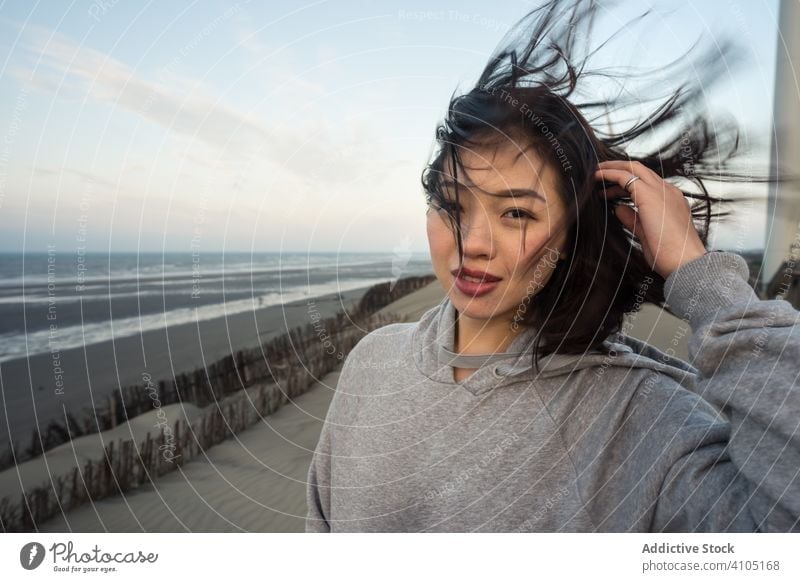 Positive asiatische Frau auf sandigen Hügeln Meeresufer Glück Windmühle Lächeln ethnisch Lachen genießend lässig reisen Urlaub aussruhen entspannend Sommer
