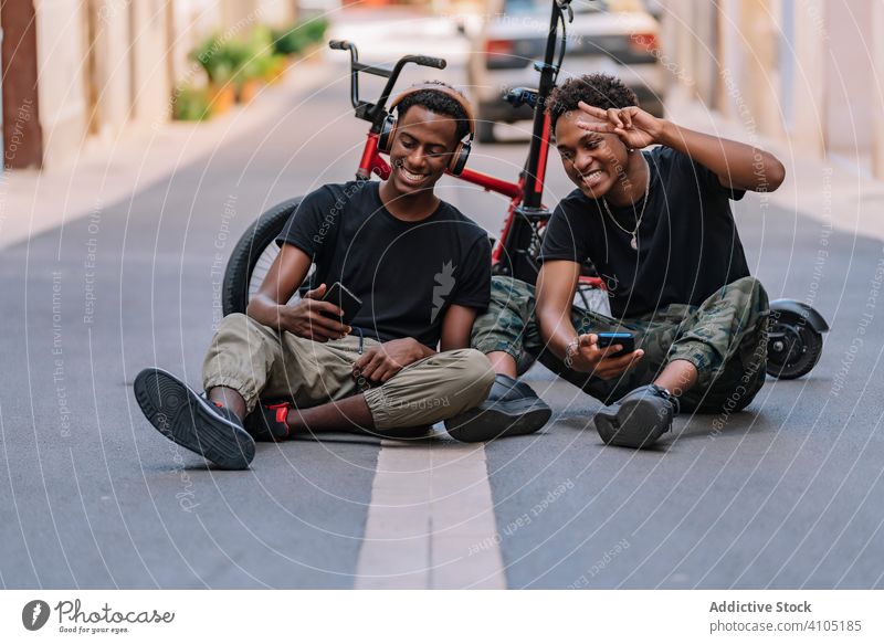 Glückliche junge schwarze männliche Hipster mit Smartphones auf der Straße Freund benutzend Generation Teenager teilen cool Bild Funktelefon Kopfhörer
