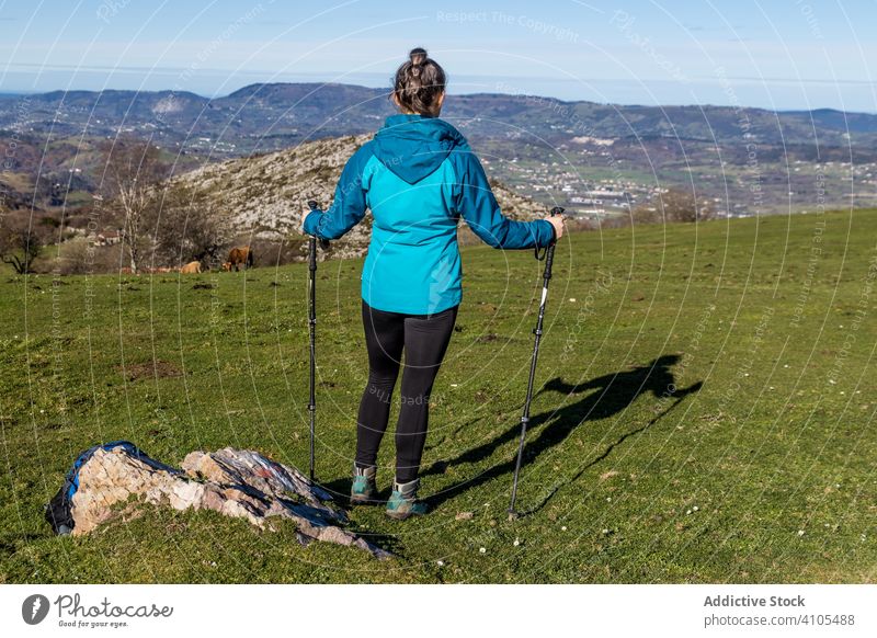 Anonyme Touristin mit Trekkingstöcken auf einer Wiese Wanderung Berge u. Gebirge benutzend Pole Hügel Felsen grün Sonnenlicht wandern Frau Sportkleidung Ausflug