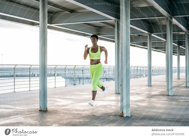 Schlanke ethnische Läuferin trainiert tagsüber auf der Straße Sportlerin laufen Training Hafengebiet Übung sportlich urban schlanke Gesundheit Motivation