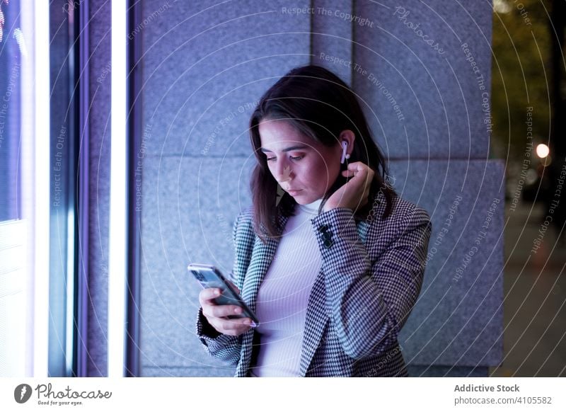 Frau mit drahtlosen Kopfhörern und Smartphone auf einer Straße in der Stadt benutzend Browsen Großstadt Drahtlos neonfarbig tws Mobile Telefon Lifestyle