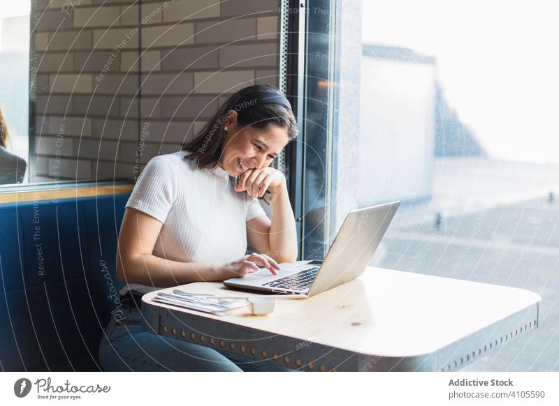 Zufriedene junge Frau lächelt, während sie in einem Café am Laptop sitzt benutzend Browsen Lächeln Lachen genießen positiv zuschauend Touchpad Anschluss