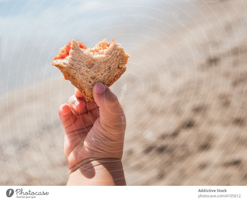 Kleines Kind hält Brot am Strand Mädchen essen Sommer sonnig tagsüber wolkig Himmel Kapuze Bekleidung Kleidungsstück Gebäck Spielfigur frisch Biss Lebensmittel