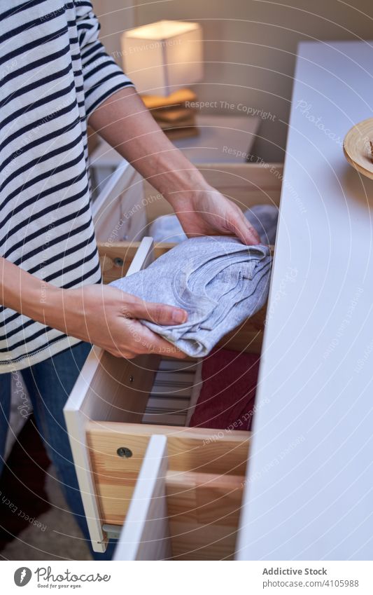 Crop Frau ordnet Kleidung in Schublade Kabinett einrichten setzen heimwärts Sauberkeit Wäscherei Routine Haushalt heimisch Appartement flach Kommode T-Shirt