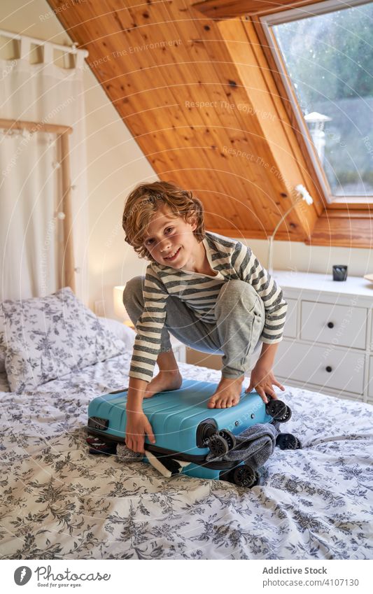 Junge sitzt auf einem Gepäckstück auf dem Bett Rudel Koffer Schlafzimmer gemütlich heimwärts obenauf sitzen Kind Feiertag Ausflug Urlaub reisen Bekleidung
