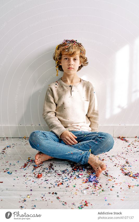 Kind in Freizeitkleidung spielt mit Konfetti zu Hause Junge heimwärts spielen männlich Teenager farbenfroh Sitzen Stock modern gekreuzte Beine Kindheit