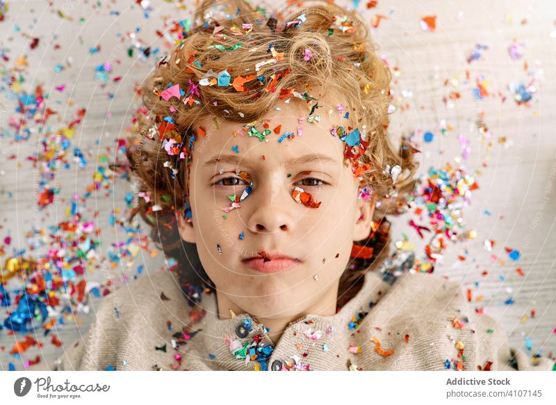 Schöner Junge mit konfettibedecktem Gesicht Konfetti heimwärts emotionslos Deckung Spaß farbenfroh Lügen Kind Stock modern Kindheit Lifestyle feiern Feiertag