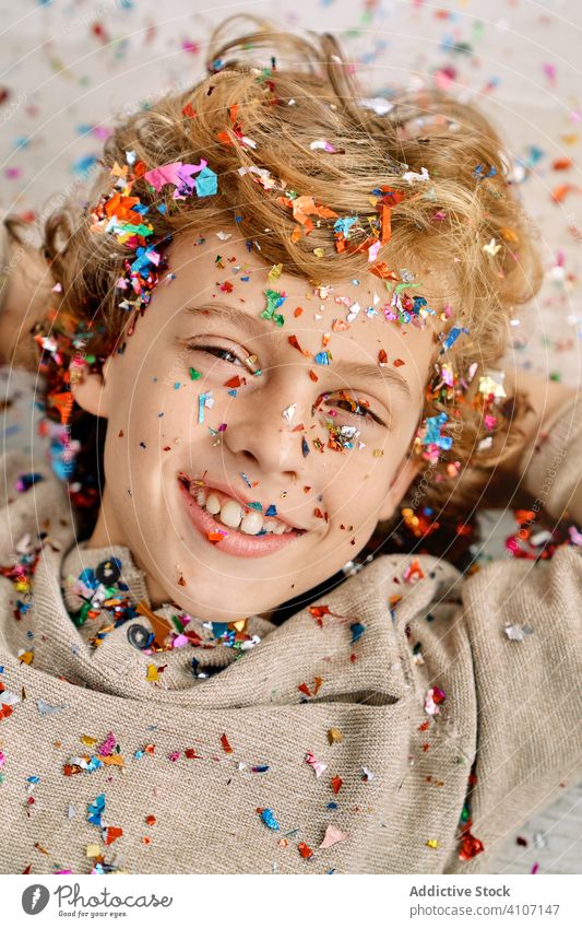 Schöner Junge mit konfettibedecktem Gesicht Konfetti heimwärts emotionslos Deckung Spaß farbenfroh Lügen Kind Stock modern Kindheit Lifestyle feiern Feiertag