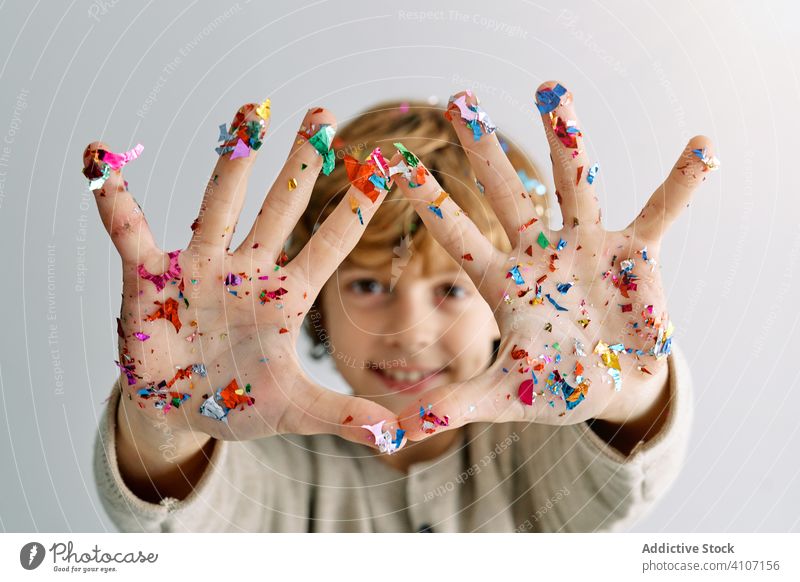 Zufriedener Junge zeigt Hände in Konfetti Hand zeigen Handfläche Kind Spaß genießen Lachen Lächeln farbenfroh Teenager manifestieren feiern Feiertag festlich