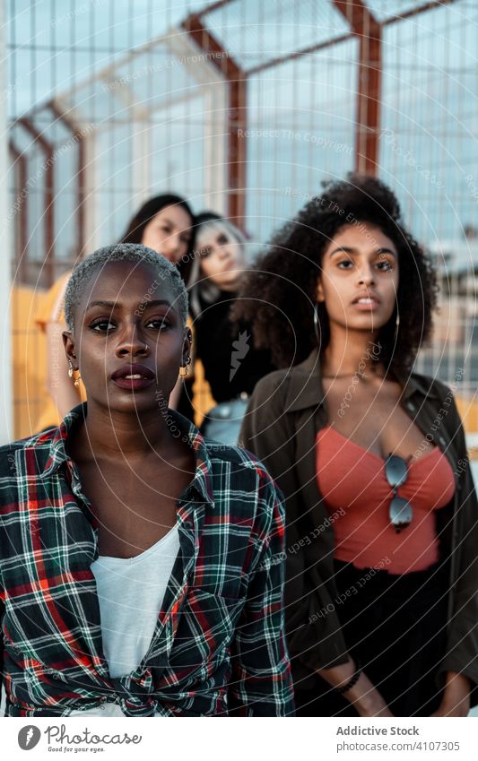 Ethnische junge Frauen in Freizeitkleidung schauen mit furchtlosen Augen in die Kamera Freund Hipster Menschengruppe ernst urban Stehen vielfältig Stil Zaun