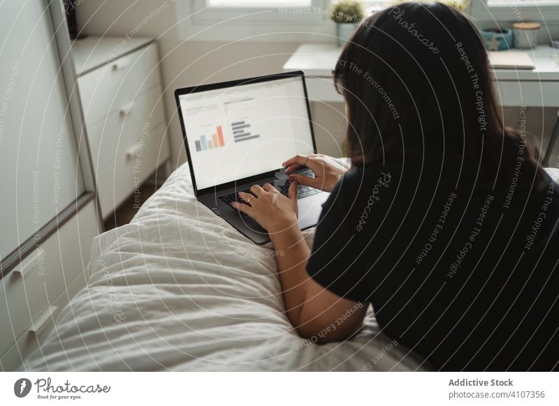 Fokussierte junge Studentin benutzt Laptop am Bett zu Hause Schüler benutzend Frau Tippen lernen Lügen Bildung Mitteilung Anschluss Kontakt Internet online