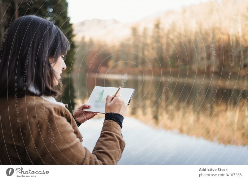 Frau steht am Seeufer und zeichnet in ein Notizbuch zeichnen Wald Landschaft ruhig Natur Herbst Bild Anstreicher malerisch jung Künstler Wasser Baum Schönheit