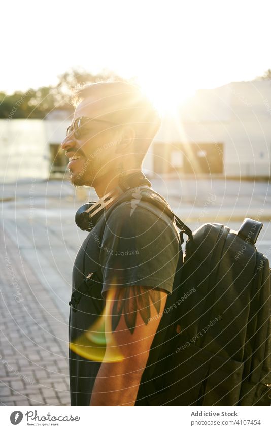 Zeitgenössischer Hispanoamerikaner auf der Straße in der Stadt Mann laufen Großstadt Sonnenuntergang Sonnenbrille lässig Kopfhörer Zubehör Rucksack Hipster