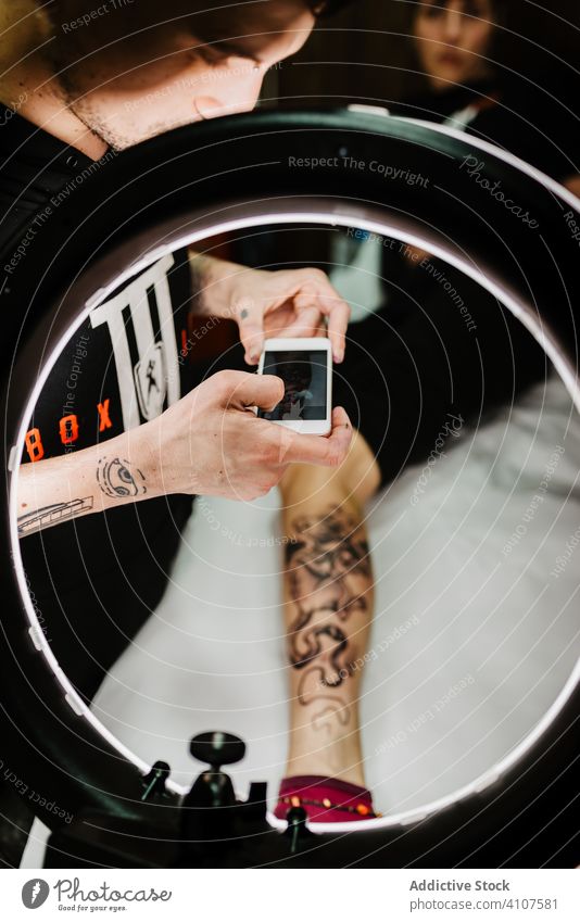 Crop-Tätowierer beim Fotografieren eines Kunden Klient fotografieren Illumination Portfolio Tattoo modern Kultur kreativ Kunst stylisch trendy Gerät Apparatur