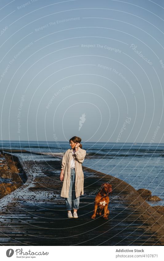 Frau mit Hund beim Spaziergang entlang der nassen Mole gegen ruhiges Meerwasser und felsige Küste bei sonnigem Wetter Pier MEER Wasser Begleiter frisch Haustier