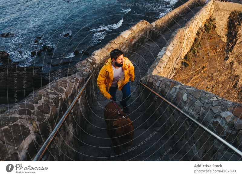 Mann mit Haustier auf Steintreppe vor felsigem Meeresufer bei Sonnenuntergang Hund Treppe Brücke Ufer Wasser MEER Küste reisen Spanien Tourismus Besitzer Dogge