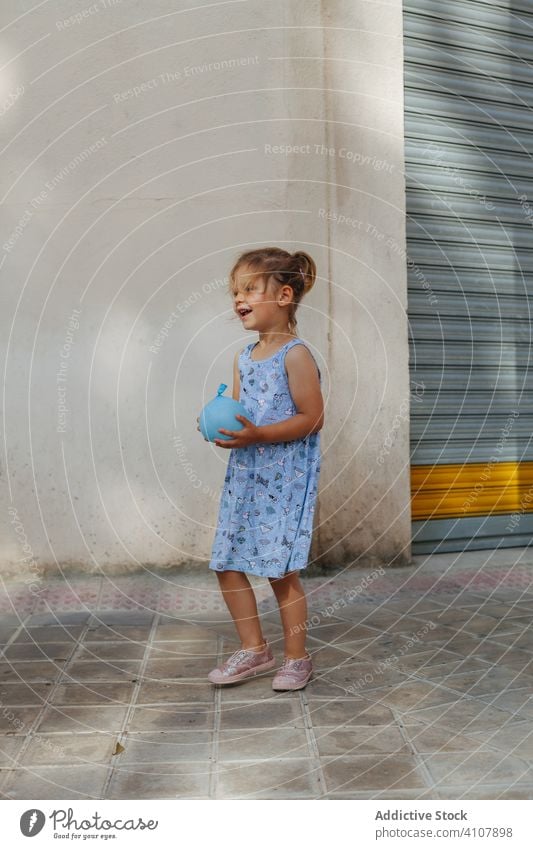 Mädchen mit Wasserballon auf der Straße Luftballon Bürgersteig Sommer Wasserbombe spielen Stadt sonnig tagsüber Kind Großstadt Straßenbelag Spielzeug niedlich