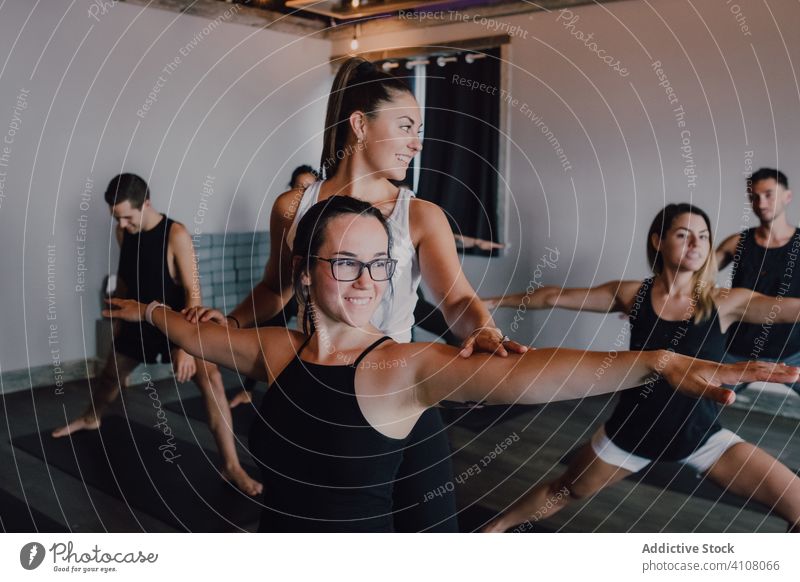 Junge sportliche Menschen, die ihren Körper dehnen und Yoga in Kriegerhaltung mit einem Trainer in einem hellen, modernen Studio praktizieren Trainerin