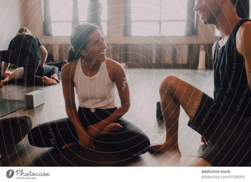 Eine Gruppe multirassischer Athleten, die sich nach einer Yoga-Übung in einem hellen, modernen Trainingsraum miteinander unterhalten und entspannen Freund
