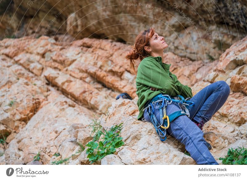 Fokussierte junge Bergsteigerin beim Ausruhen am Felsen im Sommer Alpinist Klippe Frau Aufsteiger Pause Stein extrem Herausforderung Gerät Abenteuer nachdenken