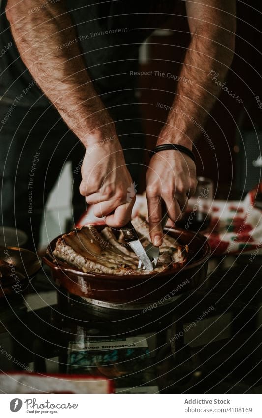 Gesichtsloser männlicher Koch, der in der Küche gebratene Rippchen mit einem Messer zubereitet Speise Fleisch Rippen Schneiden Gabel Pfanne Braten Metall