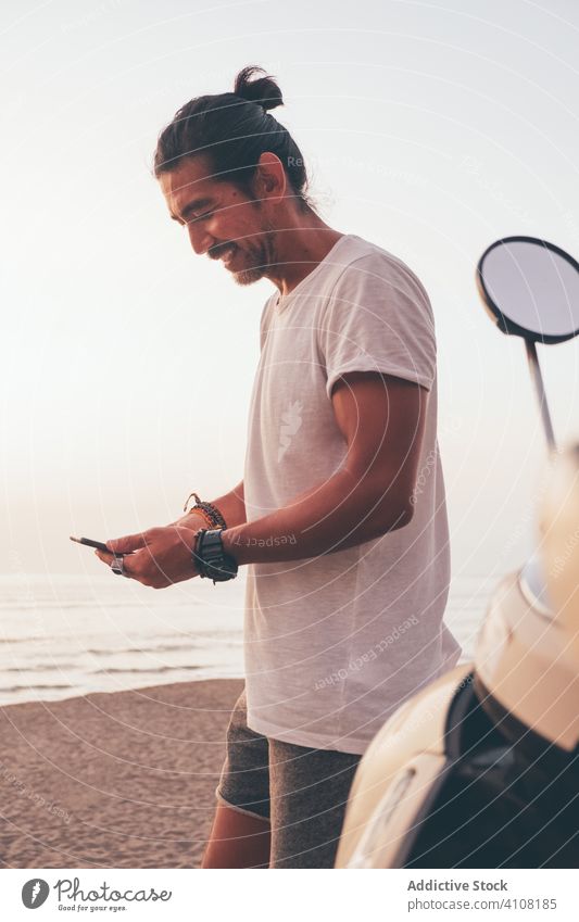 Glücklicher aktiver Mann, der am Meer telefoniert Telefon benutzend Seeküste heiter Fahrrad sportlich Smartphone männlich lässig MEER Strand ethnisch Typ