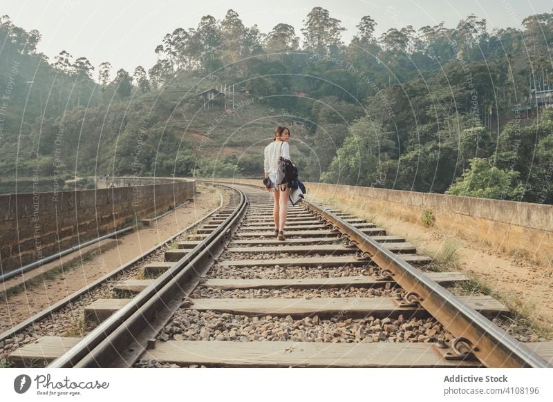 Anonymer weiblicher Tourist, der auf einer einsamen Bahnstrecke vor einem exotischen Wald spazieren geht Frau Spaziergang Eisenbahn leer grün Brücke Pflanze