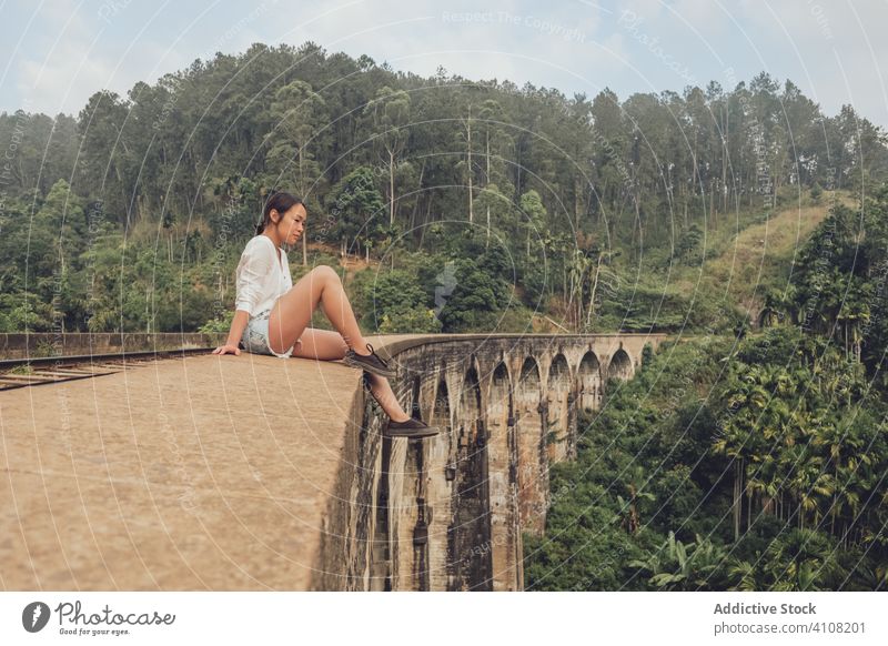 Asiatische Frau sitzt auf Eisenbahn auf Brücke in tropischer Landschaft reisen exotisch conetnt Tourismus sich[Akk] entspannen lässig grün Wald ethnisch Baum