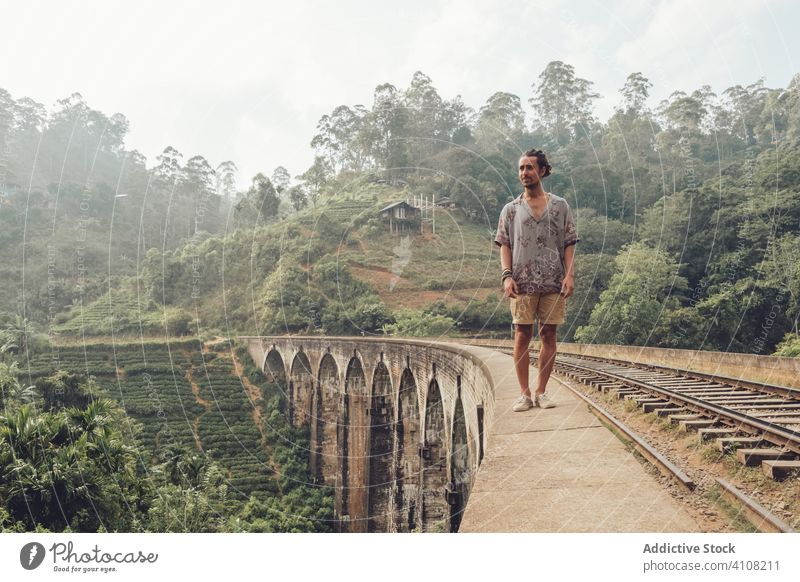 Männlicher Tourist, der auf dem Zaun einer Brücke in einer tropischen Landschaft im Nebel spazieren geht Mann Tourismus Spaziergang erkunden reisen Eisenbahn