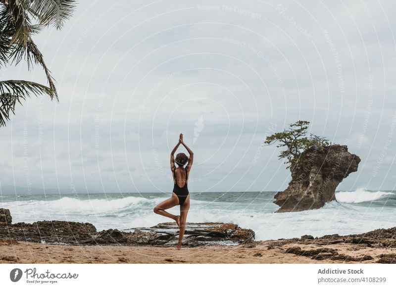 Anonyme Dame in Badekleidung beim Yoga am stürmischen Meeresufer Frau meditieren Unwetter Gleichgewicht Harmonie Kraft Strand Arm angehoben Badeanzug Freiheit