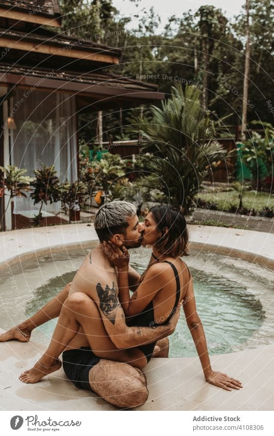 Paar im Urlaub, das sich am Pool küsst Kuss Beckenrand Resort sinnlich Hotel tropisch Flitterwochen Natur Umarmung Umarmen männlich Frau Zusammensein Badeanzug