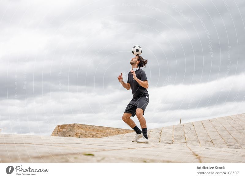 Mann trainiert mit Fußball gegen bewölkten Himmel Ball Kick wolkig Großstadt urban Straße Sport Sportler Spiel Aktivität Training Spieler Athlet Bewegung
