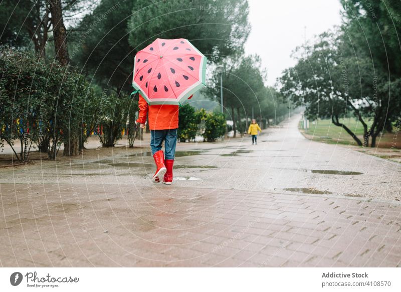 Nettes Kind mit bunten Regenschirm zu Fuß in Park Gasse Saison lustig Wasser nass Schmutz Kindheit Schlamm Herbst Spiel aktiv Wetter Gummistiefel Regenmantel